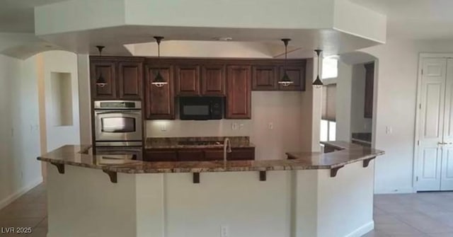 kitchen with decorative light fixtures, light tile patterned floors, black appliances, dark stone counters, and a kitchen bar