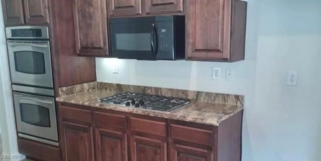 kitchen with appliances with stainless steel finishes, dark brown cabinetry, and light stone countertops