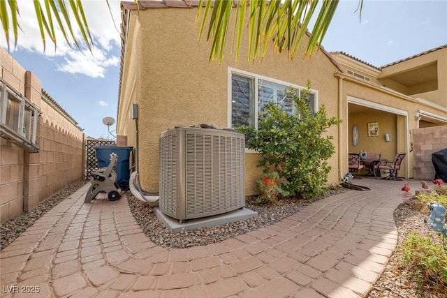 view of property exterior featuring central AC unit, fence, a patio, and stucco siding