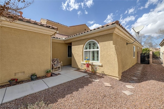 property entrance featuring a tiled roof, a gate, a patio area, and stucco siding