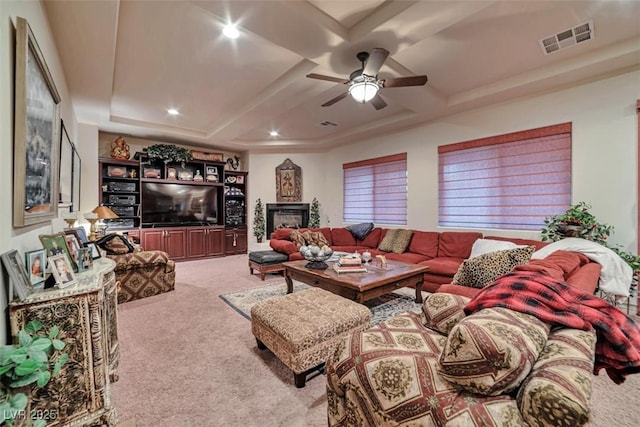 carpeted living area with coffered ceiling, a fireplace, visible vents, and a ceiling fan