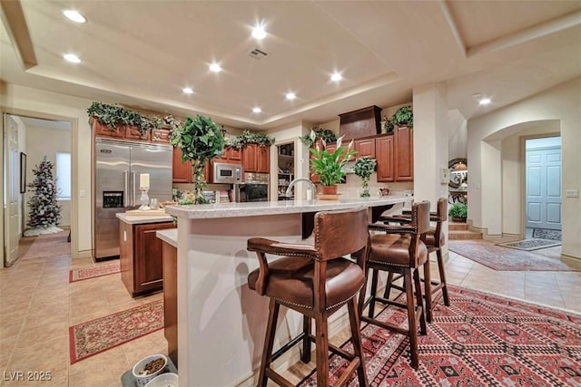 kitchen with an island with sink, a tray ceiling, and built in appliances