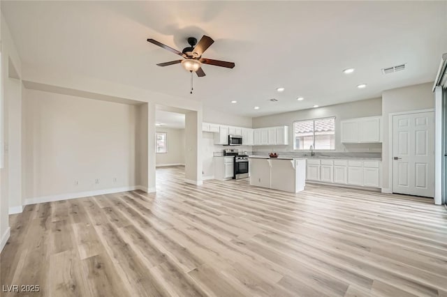 unfurnished living room featuring baseboards, visible vents, a ceiling fan, light wood-style floors, and a sink