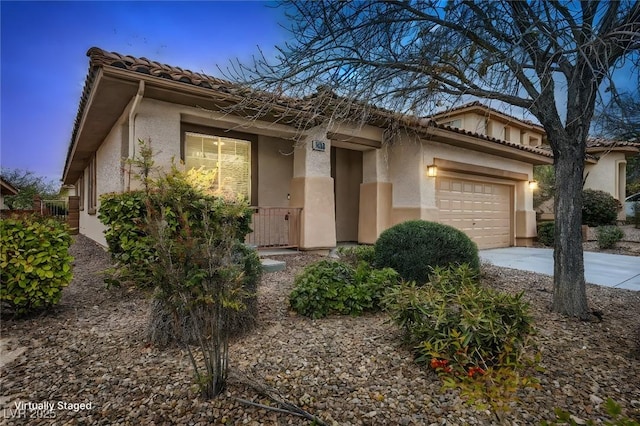 view of front of property featuring a tiled roof, an attached garage, driveway, and stucco siding