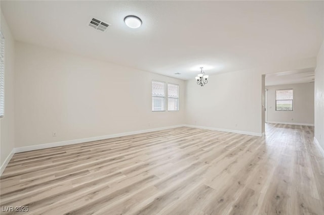 spare room with baseboards, light wood-style floors, visible vents, and an inviting chandelier