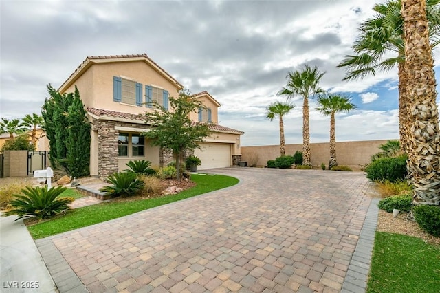 mediterranean / spanish-style home featuring decorative driveway, a tile roof, stucco siding, fence, and stone siding