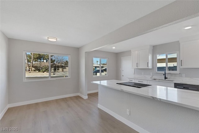 kitchen featuring baseboards, white cabinets, dishwasher, light stone counters, and a sink