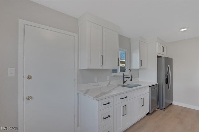 kitchen featuring stainless steel appliances, white cabinets, a sink, and light stone counters