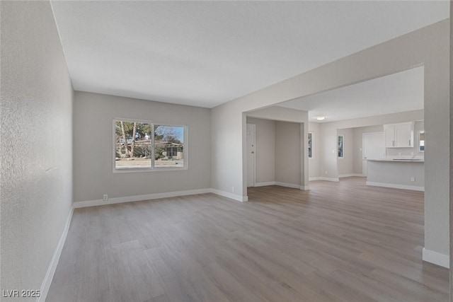 unfurnished living room with light wood-style flooring, baseboards, and a textured wall