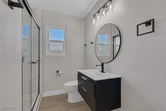 bathroom with toilet, wood finished floors, vanity, baseboards, and a stall shower