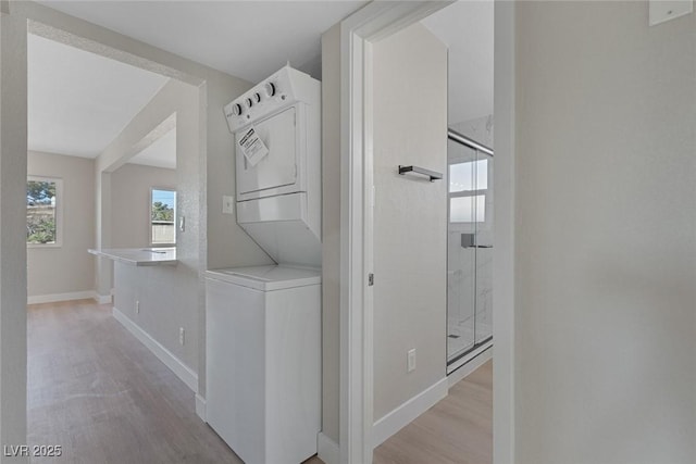 laundry room with baseboards, laundry area, light wood-style flooring, and stacked washer / drying machine