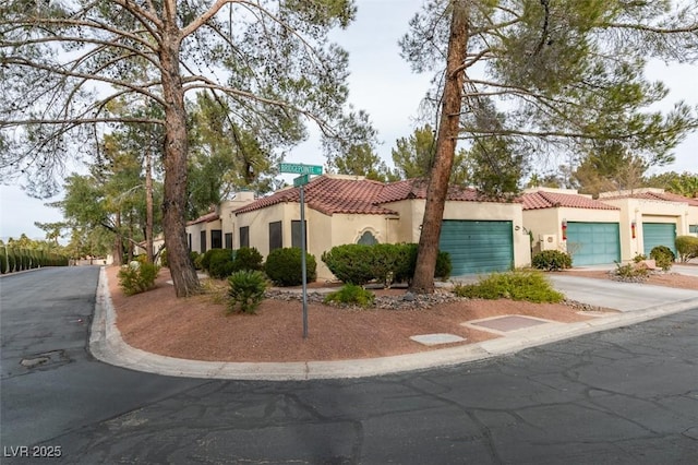 mediterranean / spanish-style house featuring a tiled roof, an attached garage, driveway, and stucco siding