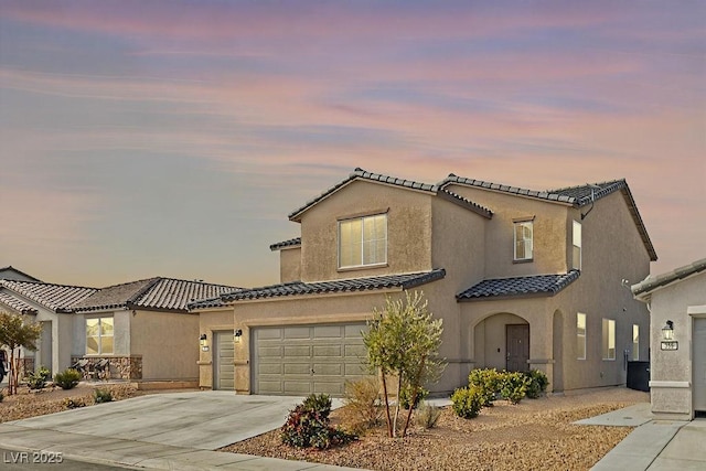 mediterranean / spanish-style house with an attached garage, a tiled roof, concrete driveway, and stucco siding