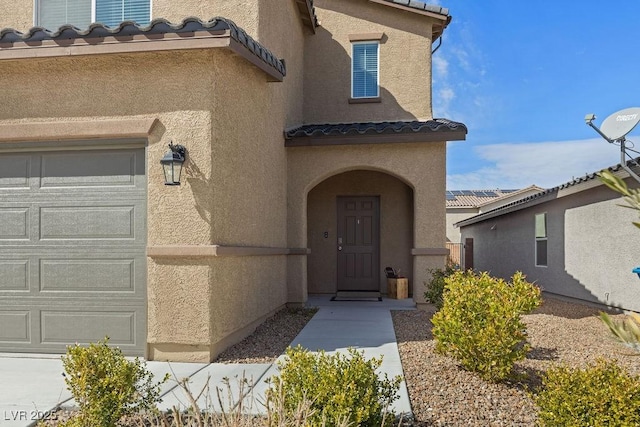 doorway to property with a garage, a tiled roof, and stucco siding