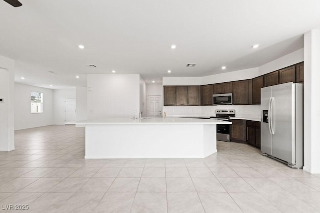 kitchen featuring stainless steel appliances, light countertops, open floor plan, a sink, and dark brown cabinets