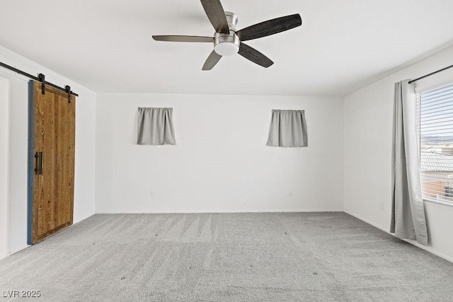 carpeted empty room with a barn door and a ceiling fan