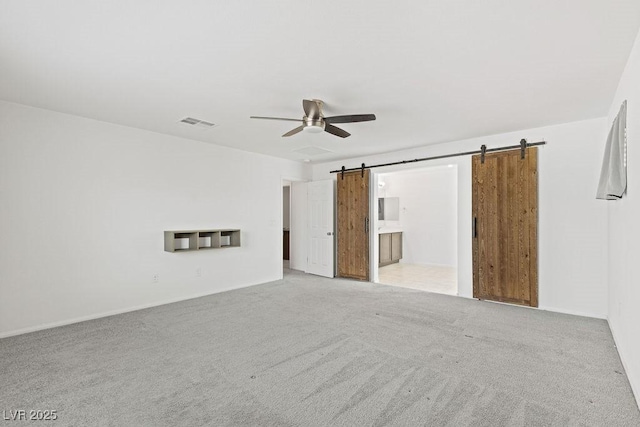 empty room featuring light carpet, ceiling fan, a barn door, and visible vents