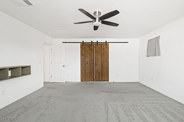 carpeted empty room with a barn door, visible vents, and a ceiling fan