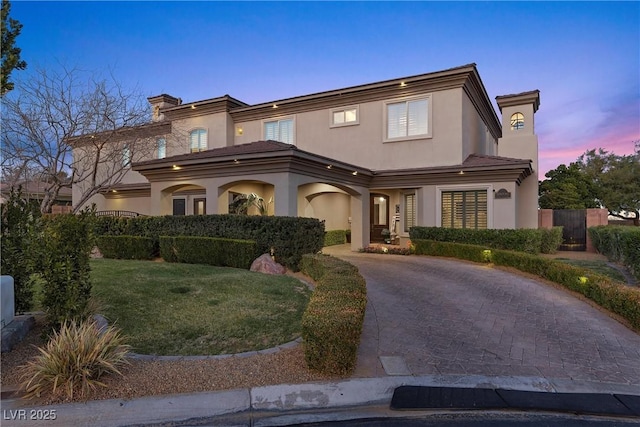 mediterranean / spanish home with a yard, a chimney, decorative driveway, and stucco siding