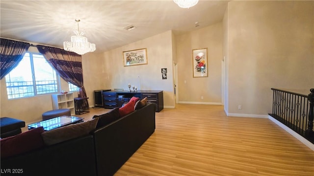 living area with visible vents, baseboards, lofted ceiling, light wood-style flooring, and a notable chandelier