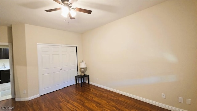 unfurnished bedroom featuring ceiling fan, a sink, baseboards, a closet, and dark wood finished floors