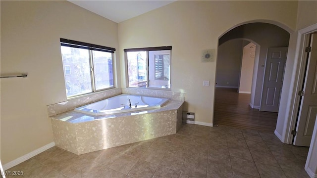 bathroom with lofted ceiling, tile patterned floors, baseboards, and a bath