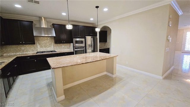 kitchen featuring arched walkways, stainless steel appliances, a kitchen island, ornamental molding, and wall chimney exhaust hood