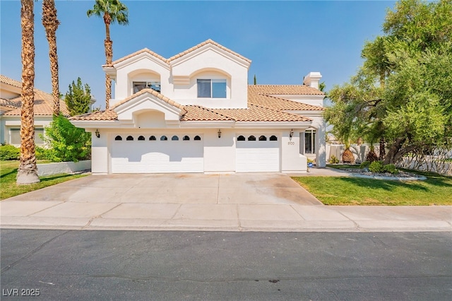 mediterranean / spanish house with a garage, fence, a tiled roof, concrete driveway, and stucco siding