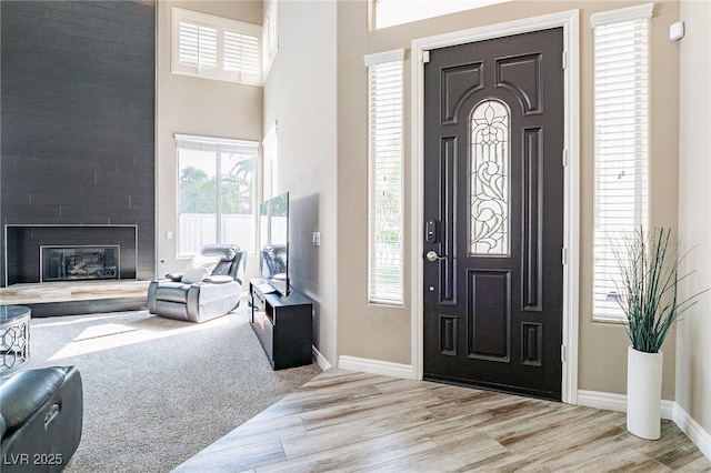 entrance foyer with a large fireplace, baseboards, a high ceiling, and wood finished floors