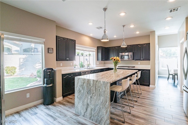 kitchen with light wood-style flooring, visible vents, a center island, stainless steel microwave, and a kitchen bar