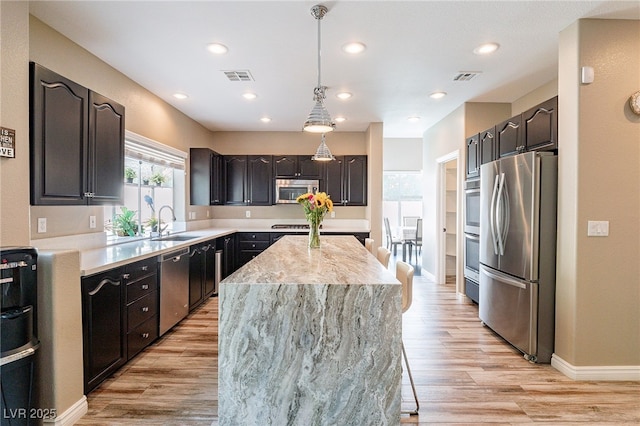 kitchen featuring visible vents, appliances with stainless steel finishes, a center island, light wood-type flooring, and a sink