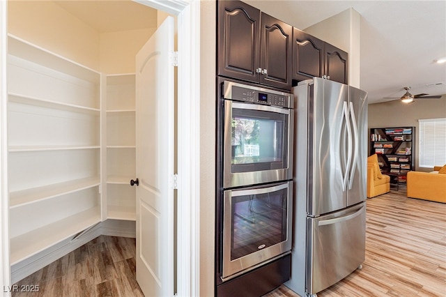 kitchen featuring dark brown cabinetry, baseboards, a ceiling fan, stainless steel appliances, and light wood-type flooring