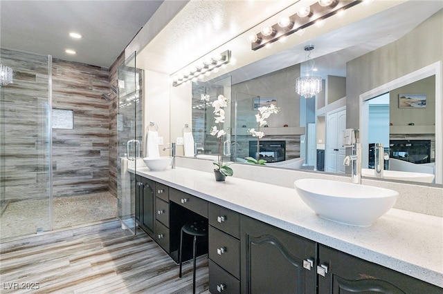 full bath featuring double vanity, a glass covered fireplace, a stall shower, and a sink