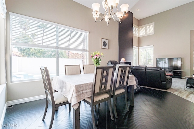 dining area featuring an inviting chandelier, wood finished floors, a towering ceiling, and baseboards