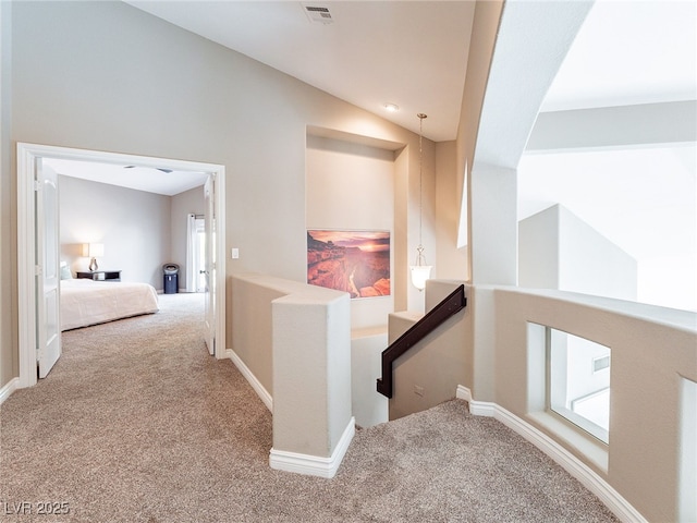 hallway with baseboards, visible vents, lofted ceiling, carpet flooring, and an upstairs landing