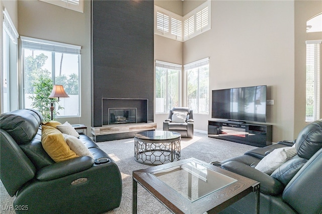 carpeted living room featuring a tile fireplace, a towering ceiling, and a healthy amount of sunlight