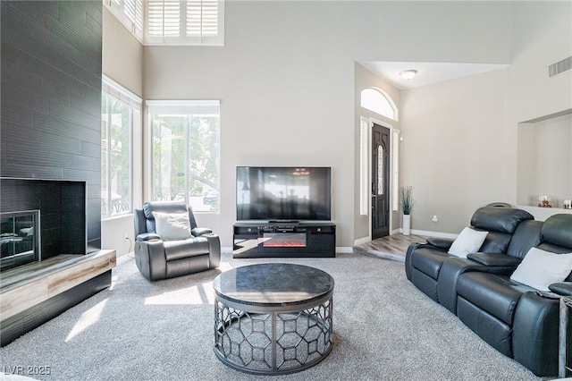 carpeted living room featuring a high ceiling, a fireplace, visible vents, and baseboards