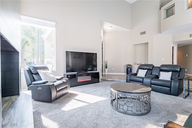 living room with baseboards, a high ceiling, visible vents, and wood finished floors