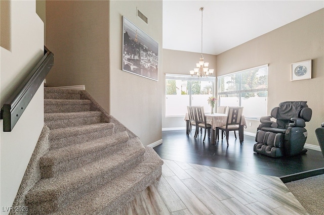 interior space with baseboards, visible vents, a towering ceiling, wood finished floors, and a chandelier