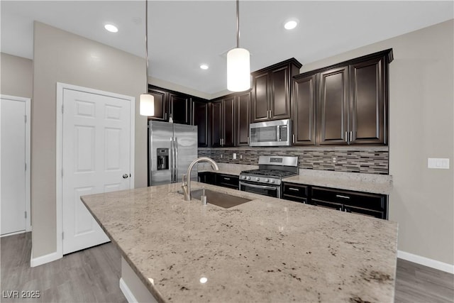 kitchen with light wood-style flooring, light stone counters, a sink, stainless steel appliances, and backsplash