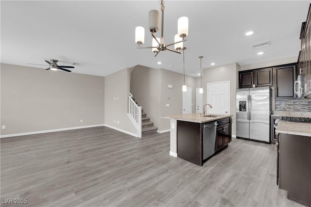 kitchen with dark brown cabinetry, a sink, open floor plan, appliances with stainless steel finishes, and a center island with sink