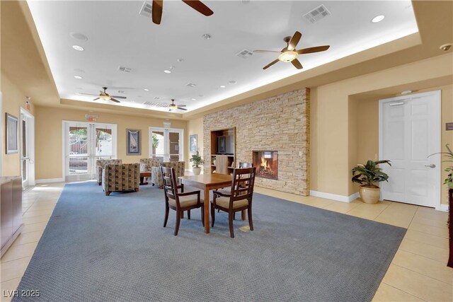 dining area featuring a tray ceiling, a stone fireplace, light tile patterned flooring, and visible vents