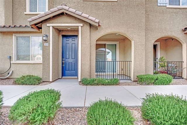 doorway to property featuring covered porch, a tiled roof, and stucco siding