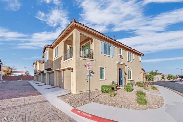 view of property exterior with stucco siding, central AC unit, a garage, driveway, and a tiled roof