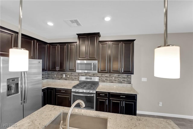 kitchen featuring light stone counters, stainless steel appliances, visible vents, decorative backsplash, and a sink