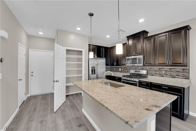 kitchen featuring light stone counters, decorative backsplash, appliances with stainless steel finishes, light wood-style floors, and a sink