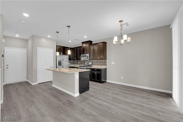 kitchen with stainless steel appliances, tasteful backsplash, a sink, light wood-type flooring, and baseboards