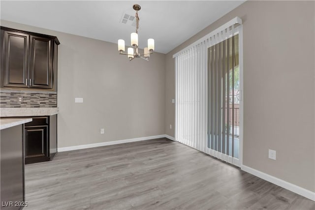 unfurnished dining area with baseboards, visible vents, light wood finished floors, and an inviting chandelier