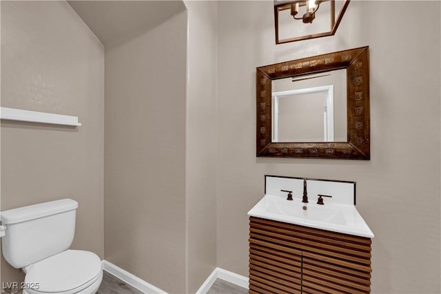 bathroom with toilet, baseboards, wood finished floors, and vanity