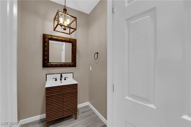 bathroom featuring a notable chandelier, vanity, baseboards, and wood finished floors